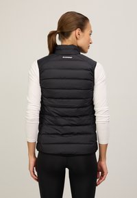Schwarze Steppweste mit vertikalen Nähten, hohem Kragen und Logo auf dem Rücken. Trägt man über einem weißen Langarmshirt und kombiniert mit schwarzen Leggings.