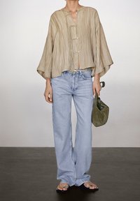 Blouse beige texturée avec un col rond et des boutons sur le devant, associée à un jean bleu clair à jambes larges. Accessoirisée d'un sac vert.