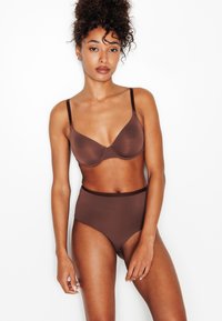 Soutien-gorge marron en tissu lisse, avec armatures et fines bretelles ajustables, assorti à une culotte marron taille haute sans coutures.