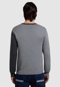 Maglione grigio con maniche lunghe, polsini a coste e scollatura rotonda. Accenti grigi più scuri sulle spalle e sulla schiena. Texture morbida.
