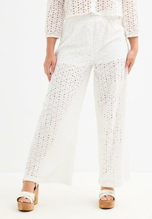Pantalones anchos blancos con un patrón de ojales, que cuentan con una cintura elástica, tejido ligero y un ajuste holgado, combinados con zapatos de plataforma en color marrón.