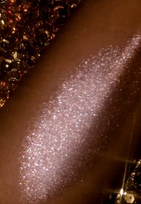 A shimmering rose gold glitter applied to skin, with fine sparkles reflecting light, against a background of textured golden sequins.