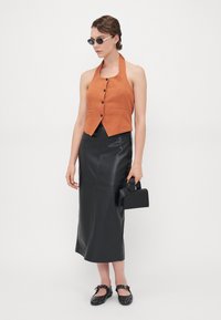 Oranje linnen haltertop met knopen, hooggesneden zwarte leren rok, zwarte handtas met strikdetail en zwarte gesp studded flats.