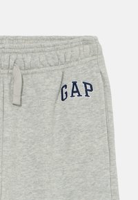 Pantalons de survêtement en coton gris clair avec une taille élastique, ornés d'une broderie "GAP" bleu marine sur le devant et d'un tissu doux et texturé.