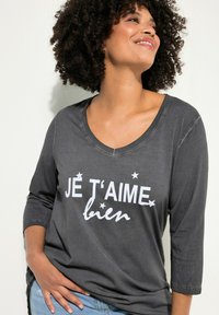 Harma pitkähihaine paita, jossa on V-pääntie ja valkoisella painettuna teksti "JE T'AIME bien", pienten tähtikoristeiden kanssa. Pehmeä kangas ja rento malli.