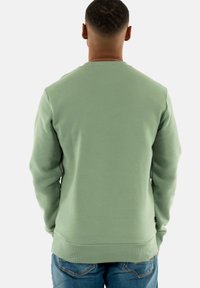 Felpa verde menta con collo a giro, polsini e orlo a coste, e una texture liscia. Indossata con jeans in denim blu.