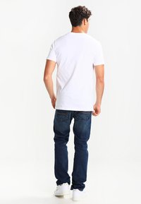 Hvit kortermet T-skjorte i bomull, rund hals; parret med mørkeblå denimjeans, rett passform, minimal detaljering, og hvite sneakers.