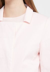 Vaaleanpunainen bleiseri, jossa on viistopartiopaita, pehmeä rakenne ja hienovaraiset ompeluyksityiskohdat. Suunnittelu on räätälöity siistin ilmeen saavuttamiseksi.