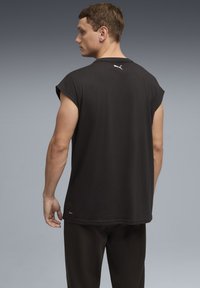 T-shirt noir sans manches en tissu doux, avec coutures d'épaule roulées, un petit logo blanc au dos, et une coupe décontractée.