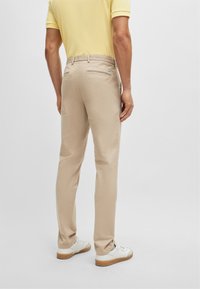 Beige trousers with a slim fit, made of smooth fabric. Features a back pocket and a belt loop. Worn with white sneakers.