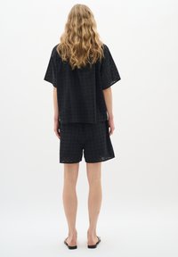 Top nero a maniche corte e pantaloni abbinati realizzati in tessuto perforato. Caratterizzato da una vestibilità ampia con ritagli quadrati e hardware minimale. Sandali piatti.
