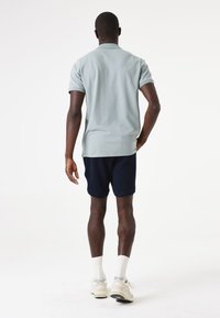 Camisa polo verde claro de manga corta combinada con pantalones cortos texturizados en navy, completada con calcetines deportivos blancos y zapatillas beige.