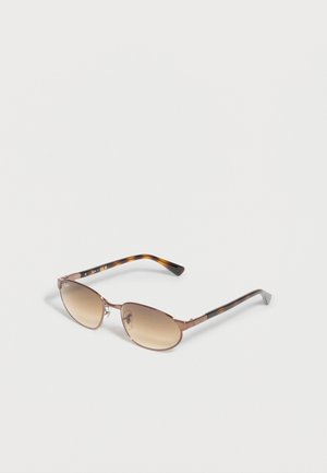 Ruskeat metallikehyksiset aurinkolasit, joissa on soikeat liukuvärjätyt ruskeat linssit ja kilpikonnakuviolliset sankat, lepäävät vaaleanharmaalla pinnalla.