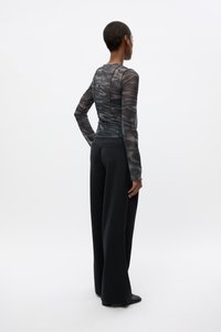 Black sheer long-sleeve top with a subtle patterned design, paired with high-waisted black wide-leg trousers. Smooth texture, fitted style.