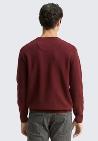 Burgunderfarbener Strickpullover mit Rundhalsausschnitt, gerippten Bündchen und Saum. Das Material hat eine strukturierte Oberfläche. Die Rückansicht zeigt ein schlichtes Design.