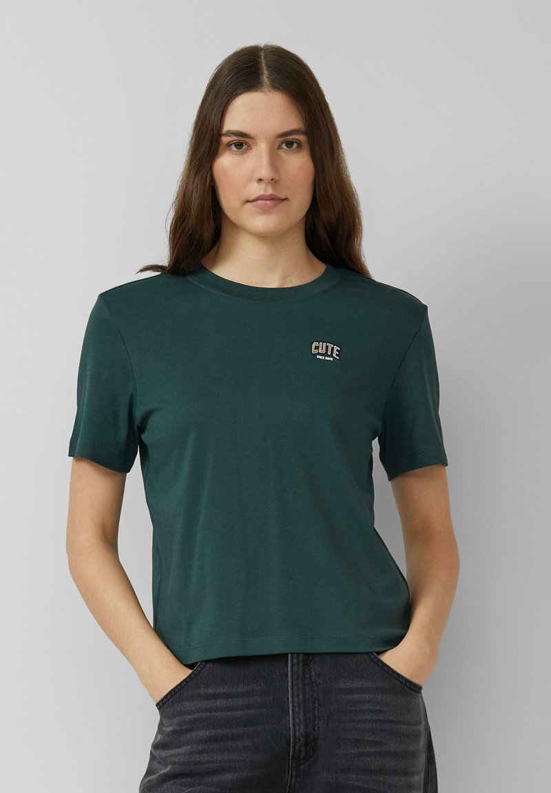 Donkergroen t-shirt met korte mouwen gemaakt van zachte stof, voorzien van een klein geborduurd "CUTE" logo op de linker borst. Eenvoudig ontwerp en pasvorm.