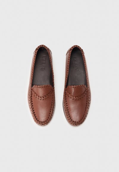 Paire de mocassins en cuir marron avec couture mocassin autour des bords, présentée côte à côte sur un fond blanc.