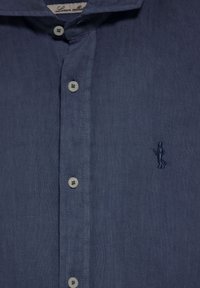 Donkerblauwe linnen shirt met een knoopsluiting aan de voorkant, een klassieke kraag en een klein geborduurd figuurtje aan de linkerkant. Zachte textuur.