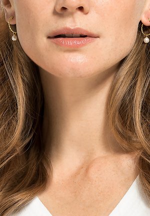 Goldene Creolen mit einem gedrehten Design, versehen mit einer kleinen weißen Perle, die von jeder hängt. Glatte Oberfläche und subtiler Glanz.