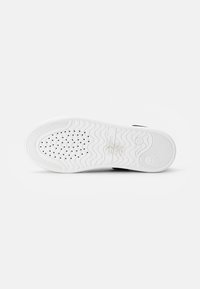 Suela de zapatilla blanca con patrón texturizado; presenta perforaciones circulares y un diseño ondulado. Incluye un logo en relieve y material de goma flexible.