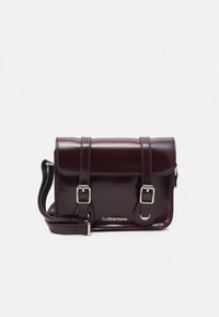 Kompaktní crossbody kabelka z vínově červené kůže s lesklým povrchem, dvojitými přezkami a stříbrným kováním. Má nastavitelný popruh.