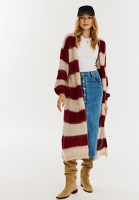 Pletený kardigan s červenými a béžovými pásmi, voľný strih, otvorený predok. Skombinovaný s bielym topom a džínsovou sukňou modrej farby s gombíkmi.