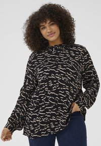 Blouse à manches longues noire avec des motifs abstraits beiges, présentant un col haut et une texture froncée, conçue pour un ajustement ample.