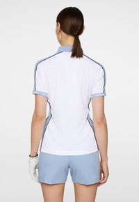 Vit pikétröja med ljusblå accenter och detaljer, i kombination med ljusblå shorts. Har en strukturerad krage och korta ärmar.