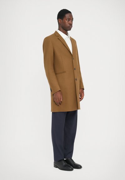 Palton din lână maro cu un design cu un singur rând de nasturi, revere cu notch și două buzunare frontale, asortat cu pantaloni bleumarin și pantofi negri.