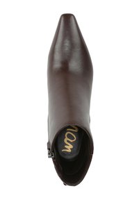 Bottine en cuir marron avec un bout pointu, texture lisse, fermeture éclair latérale et une semelle intérieure noire avec des lettres dorées.