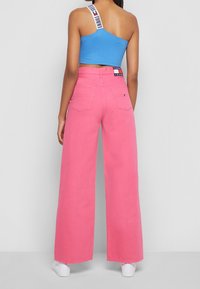 Vidaffa rosa jeans med vida ben, hög midja och två bakfickor, kombinerat med en blå crop top med ett vitt band med varumärkeslogotyp.