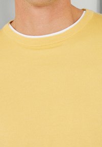 Camiseta de algodón amarilla con cuello redondo, con una textura acanalada y un cuello interior blanco en capas para un detalle adicional.