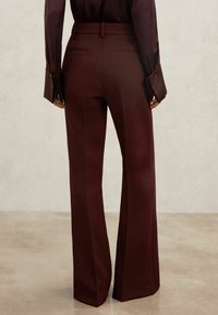Pantalones de pierna ancha color granate con una textura suave, con cintura de altura media, trabillas para cinturón y dos bolsillos traseros.