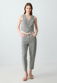 Gilet corto a righe grigie e bianche con bottoni abbinato a pantaloni tapered. Il modello indossa sandali flat, dal design minimalista.