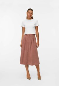 Haut blanc à manches courtes associé à une jupe A-line rose pâle avec un bouton à la taille et des plis, complété par des escarpins à motifs.