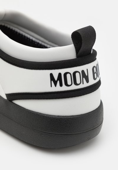 Adidași alb-negru cu un material neted, formă rotundă și textul proeminent "MOON BOOT" pe călcâi. Dispune de o talpă texturată de culoare neagră.