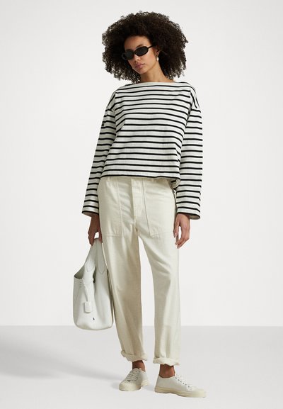 Haut à rayures noir et blanc à manches longues, pantalon crème fuselé, baskets blanches et sac à main blanc. Tissu texturé, design décontracté.