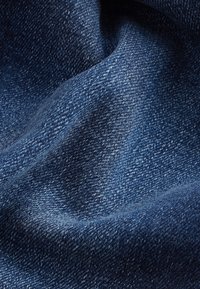 Gros plan sur un tissu en denim bleu foncé montrant le tissage détaillé et la texture avec des plis naturels et des ombres.