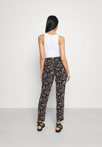 Black patterned pants with a floral design, paired with a white sleeveless top. Features a relaxed fit and ankle-length cut with straps on sandals.