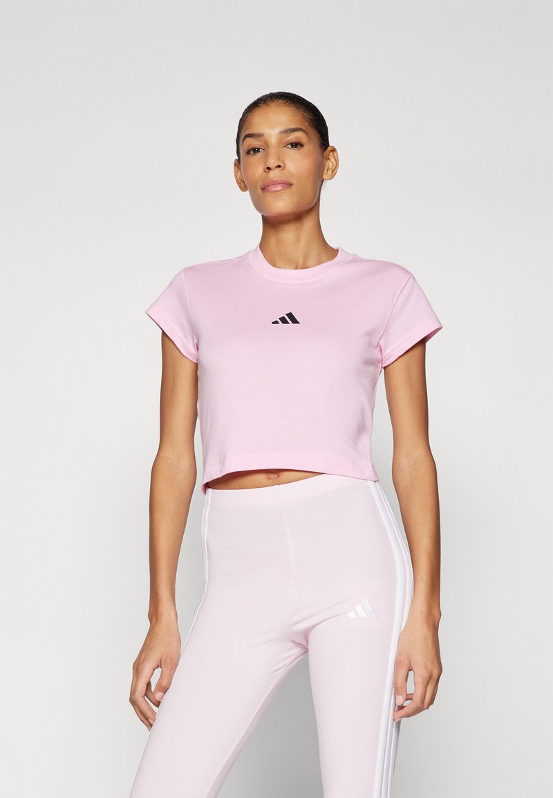 Pink cropped t-shirt made of soft cotton, featuring short sleeves and a black Adidas logo centered on the chest, paired with matching pink leggings.