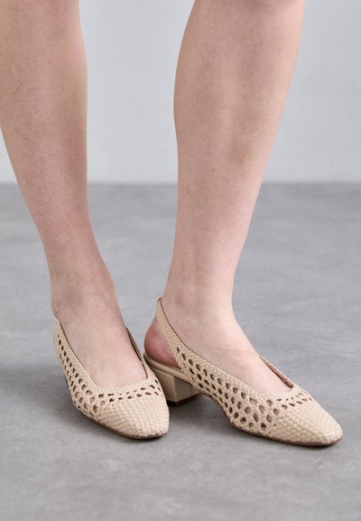 Beige tkané šlapky se špičatou špičkou a malým blokovým podpatkem. Mají otevřenou stranu a texturovaný povrch.