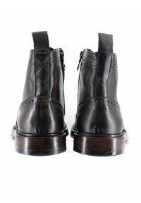 Stivali alla caviglia in pelle nera con finitura liscia, zip laterali, dettagli brogue e tacco in legno impilato.