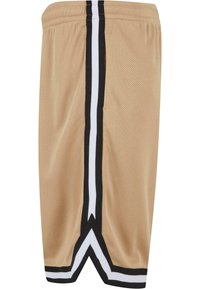 Shorts en mesh beige avec une bande verticale noire et blanche sur les côtés et un ourlet en forme de V en bas.