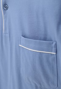 Camicia azzurro chiaro con chiusura a bottoni e taschino sul petto, caratterizzata da piping bianco lungo il bordo della tasca. Tessuto morbido.