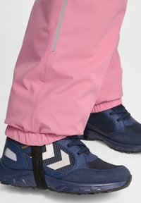 Blauwe sportieve schoenen met zwarte en witte accenten, gecombineerd met roze waterbestendige broek, voorzien van verstelbare elastische manchetten en reflecterende details.