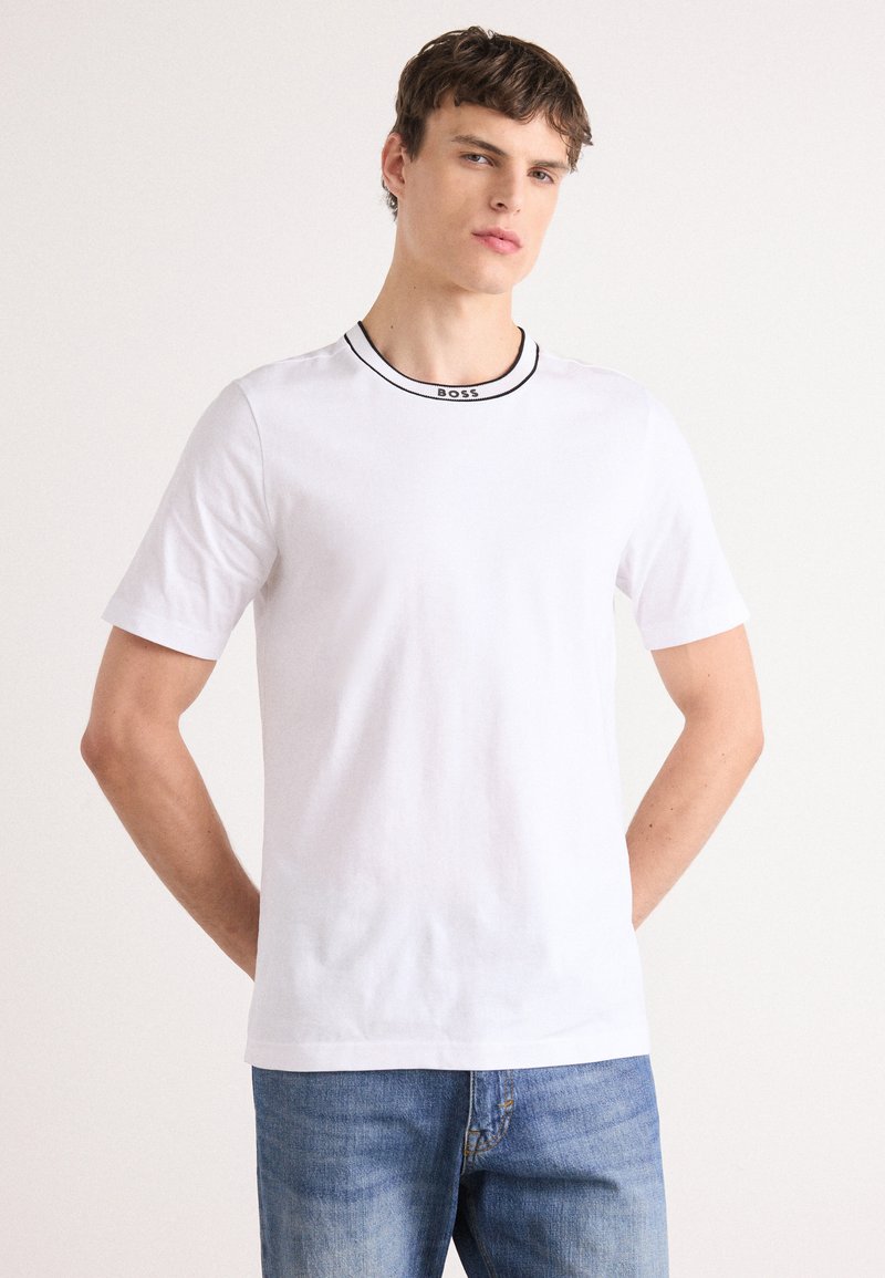 Hvid kortærmet T-shirt lavet af bomuld, med et sort kantet rund halsudskæring og "BOSS" logo detaljer. Minimalistisk design med en afslappet pasform.