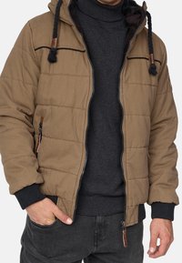 Braune wattierte Jacke mit Kapuze, Reißverschluss und schwarzen Akzenten. Verfügt über Reißverschlusstaschen und gerippte Bündchen für Wärme.