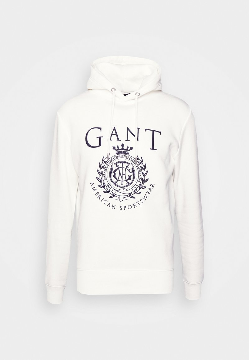 Sweat à capuche blanc avec logo GANT et écusson bleu marine, avec cordons de serrage et manches longues.