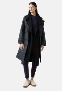 Prošívaný černý kabát s klopovým límcem, dlouhými rukávy a otevřeným předním dílem. Nosený přes tmavý top a námořnické kalhoty, doplněný světlými botami.