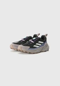 Des chaussures de trail noires et violettes présentent un dessus texturé, trois rayures blanches et une semelle robuste avec des crampons prononcés pour une meilleure adhérence.